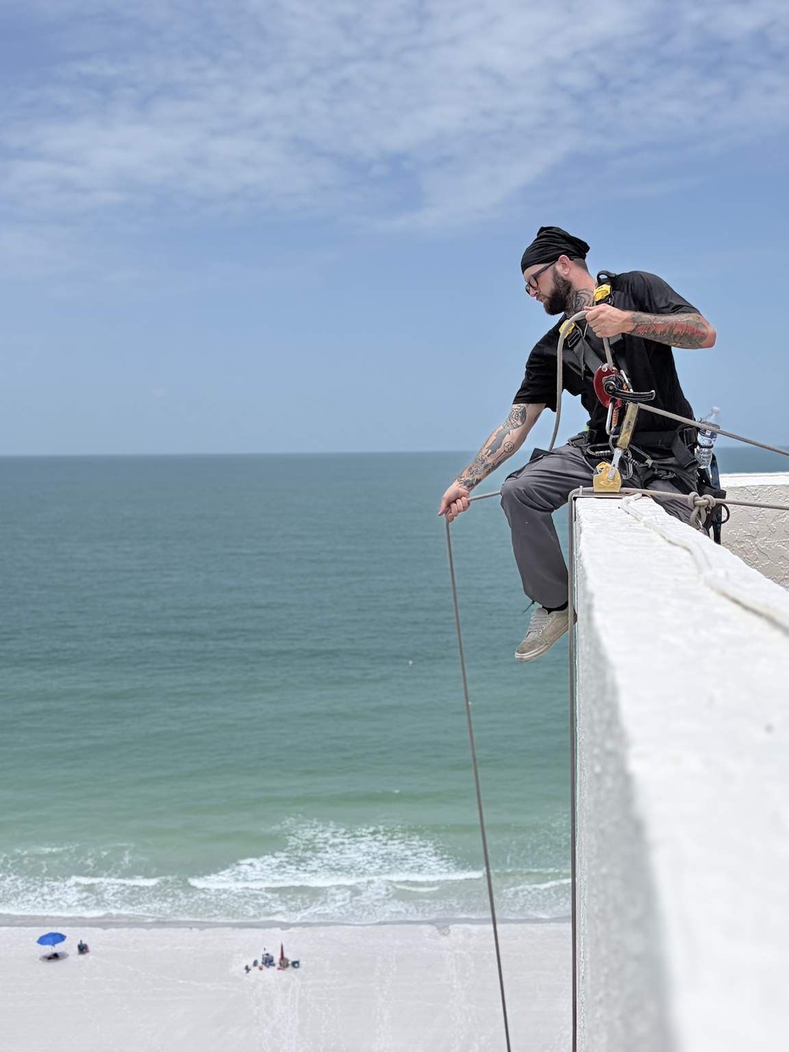 Window cleaner preparing rope-access equipment above the beach
